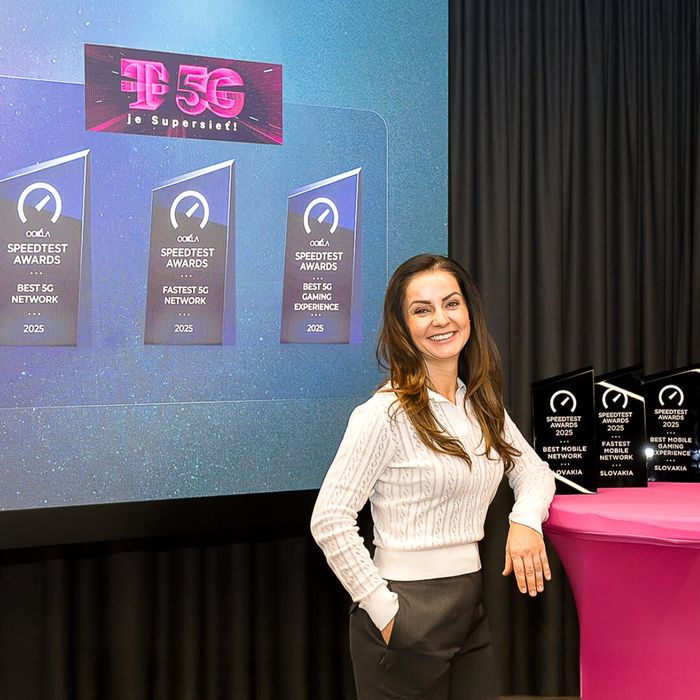 Žena sa usmieva vedľa vystavených telekomunikačných ocenení vrátane ocenenia „Najlepšia 5G sieť“. Na obrazovke sa zobrazujú ocenenia za 5G a na stole sú ďalšie trofeje.