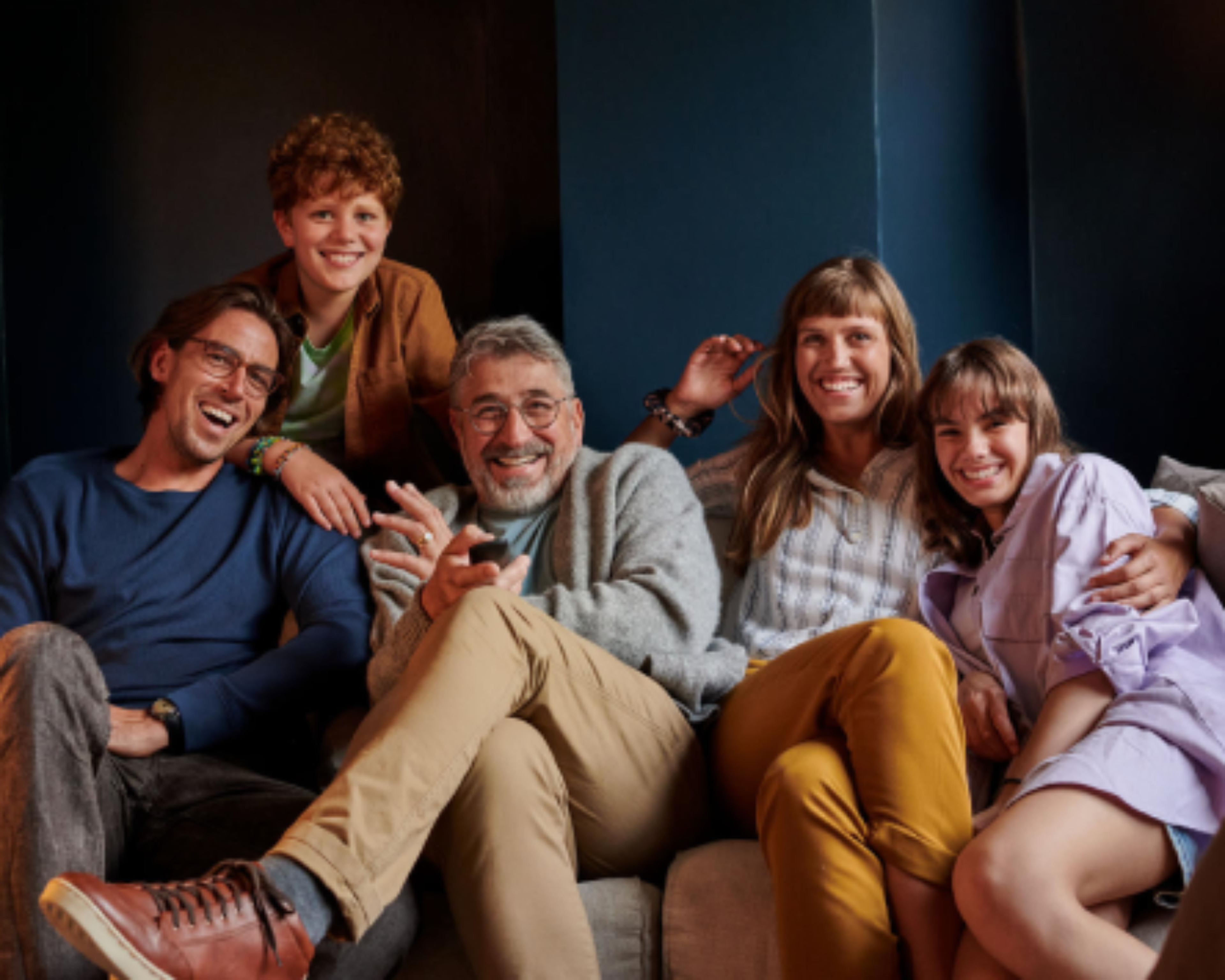 Usmiata rodina sediaca spolu na pohovke, šťastne pozerajúca do kamery.