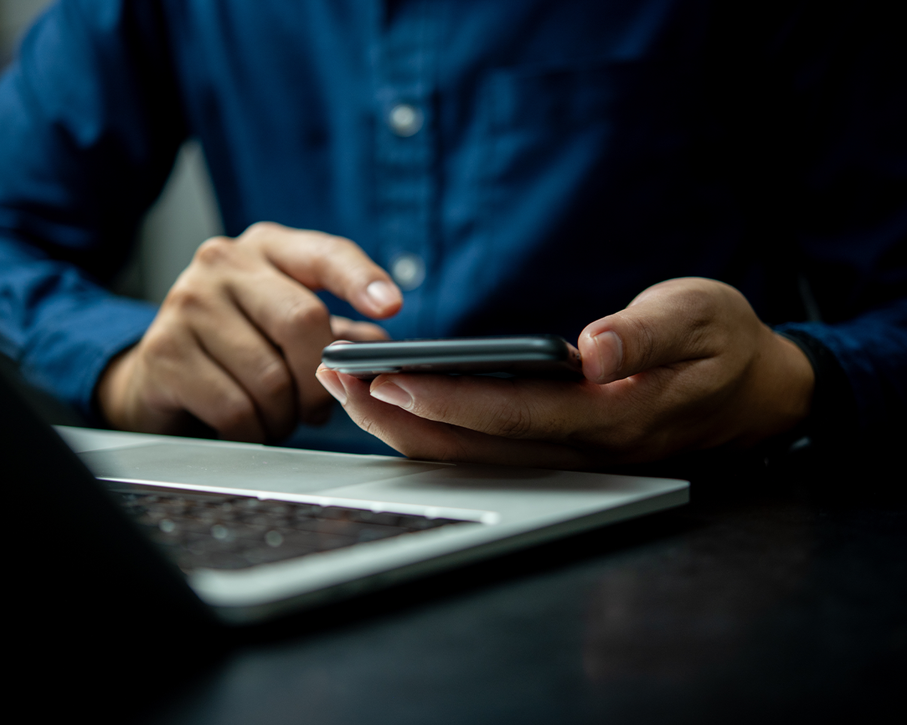 Detail na otvorený notebook a ruky držiace mobil