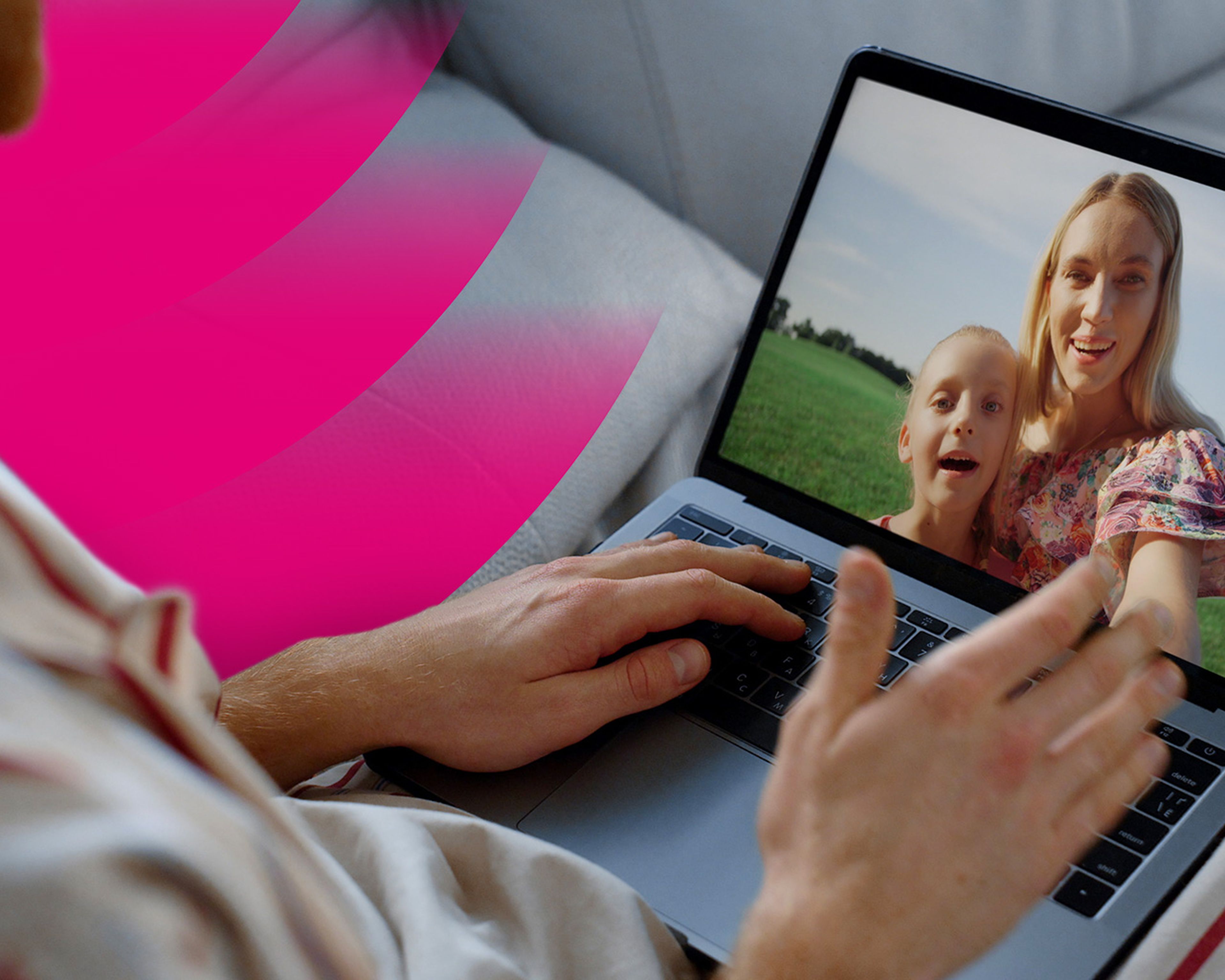 Osoba vedie videohovor na notebooku so ženou a dieťaťom na poli na ružovo-bielom pozadí.