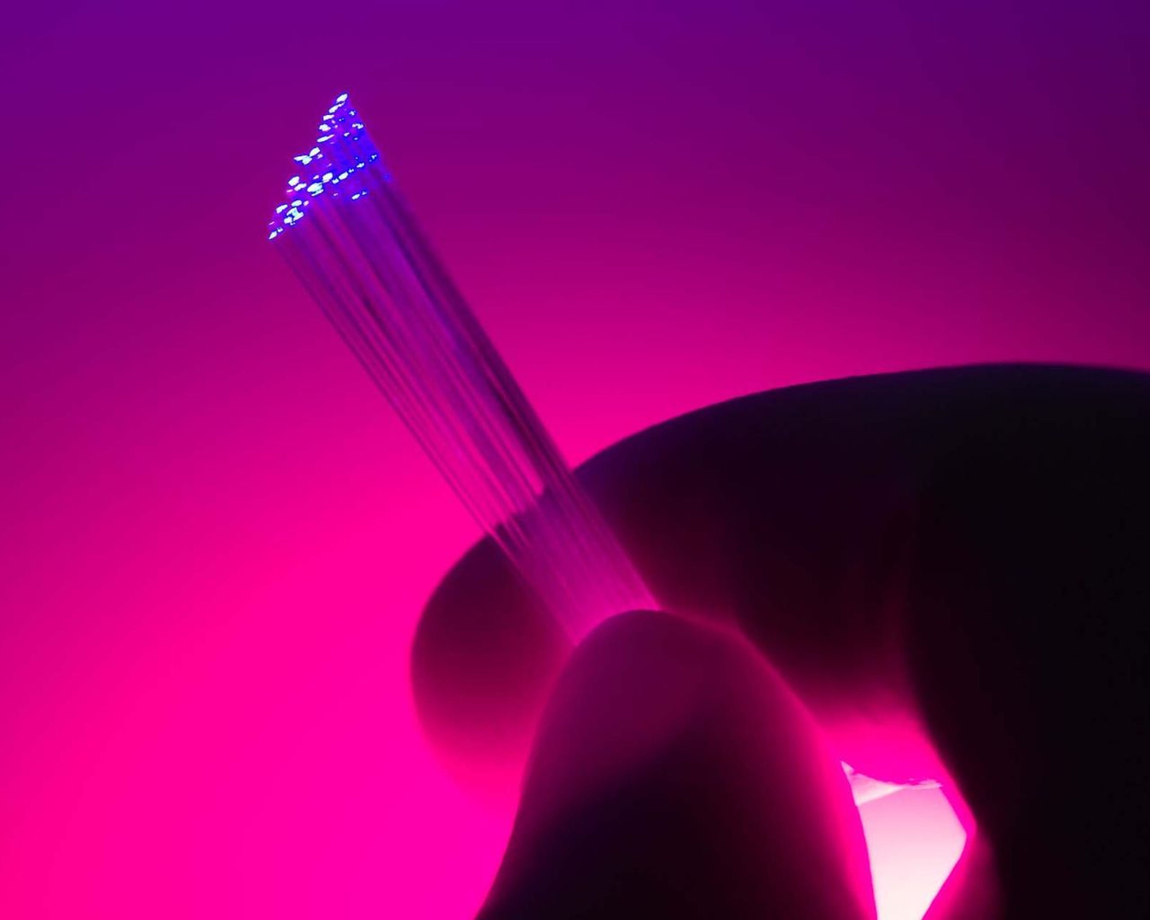 Detailný záber ruky držiacej žiariace optické vlákna na žiarivo ružovom a fialovom pozadí.