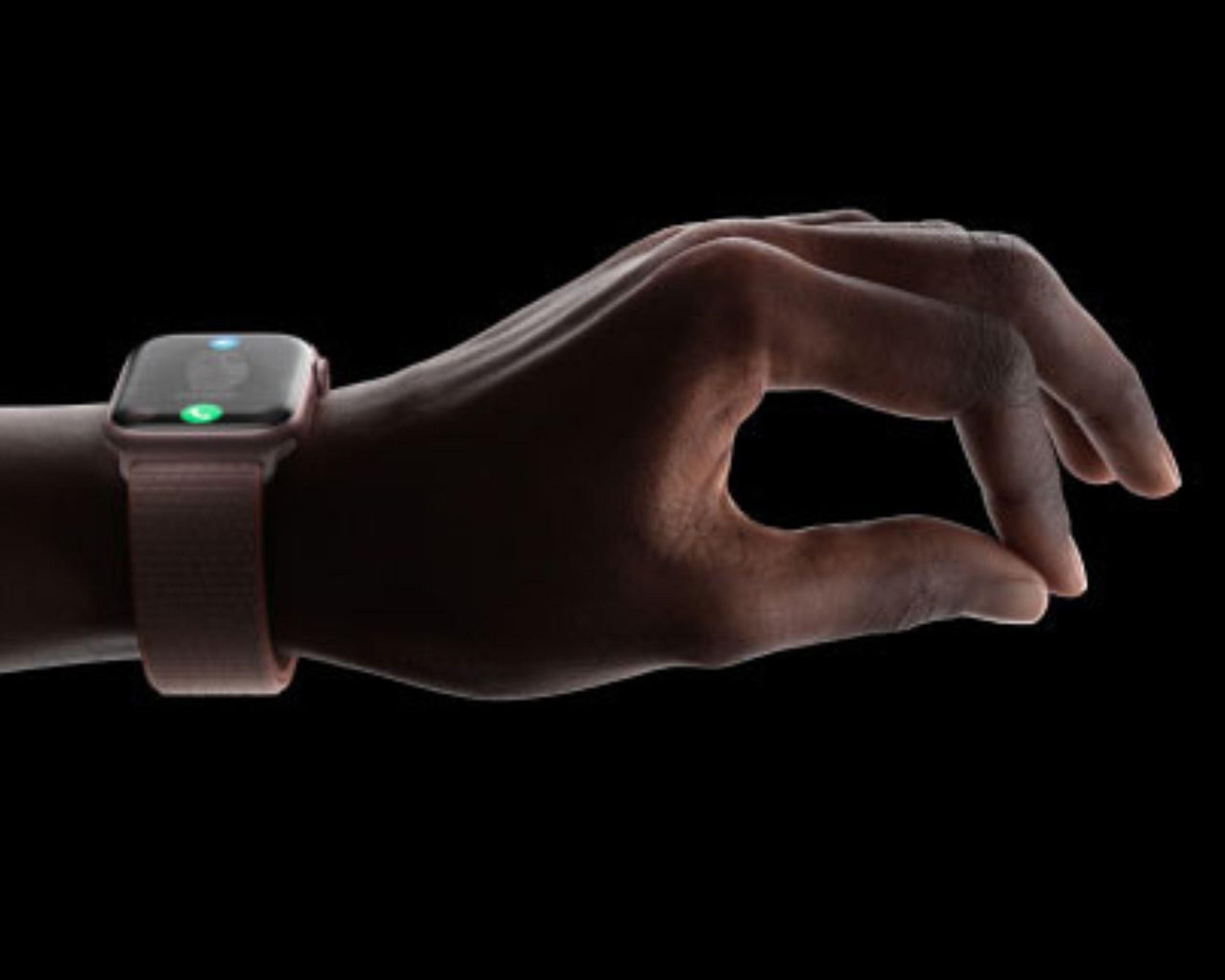 Ruka s inteligentnými hodinkami s ružovým remienkom gestikuluje na čiernom pozadí. Obrazovka hodiniek zobrazuje ikony.