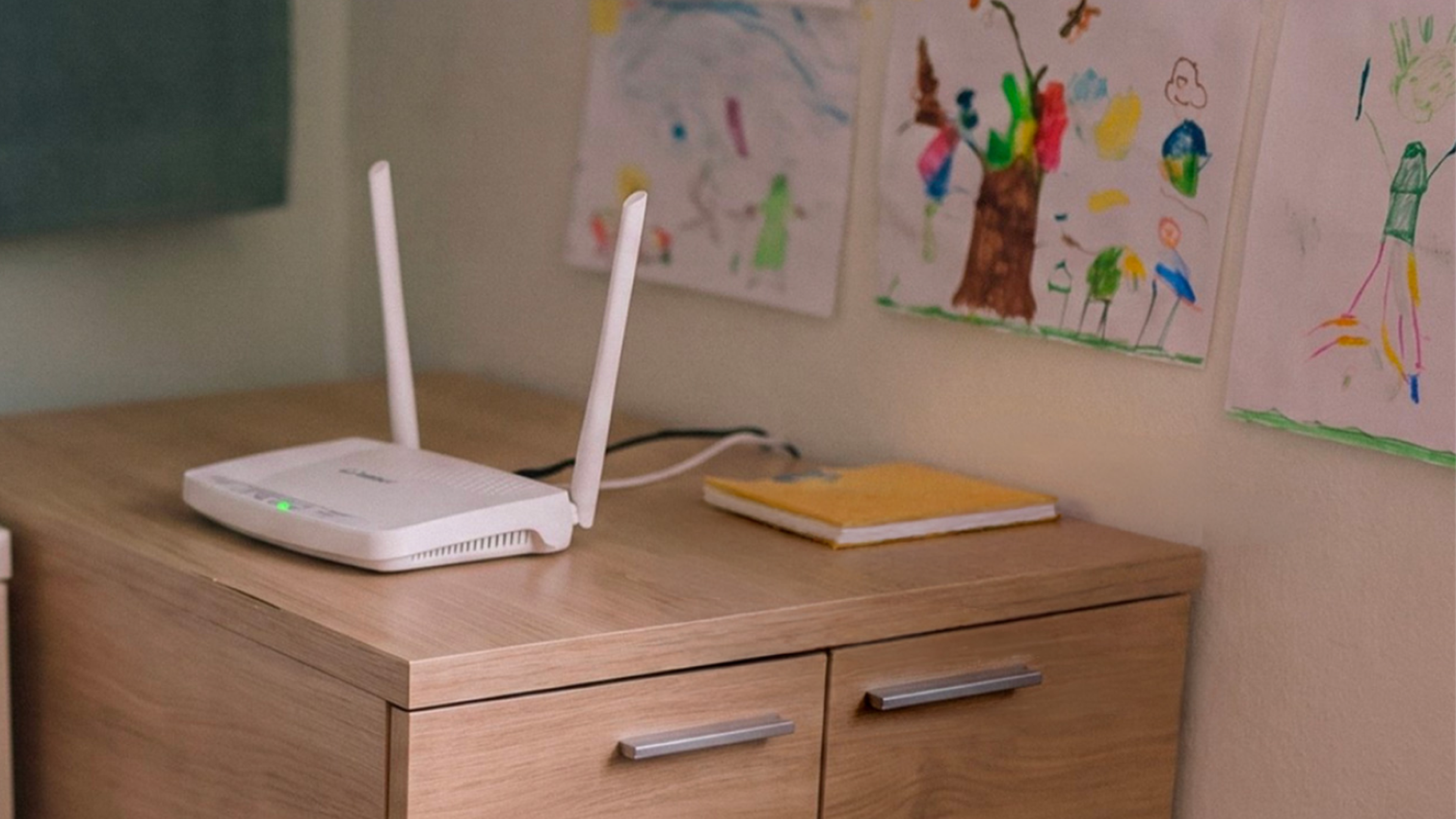 WiFi router na drevenej komode, v pozadí detské kresby na stene.