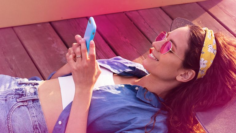 mladá usmiata brunetka ležiaca v lete vonku na slnku pozerá do mobilu