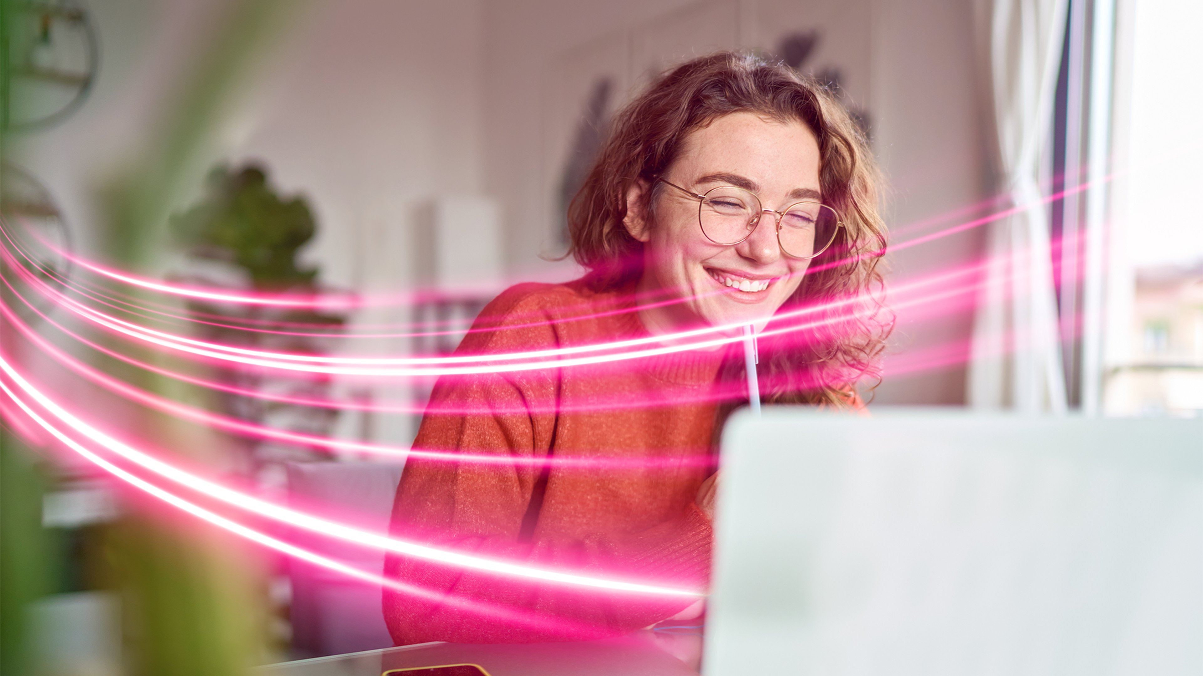 Žena so šťastným výrazom pracujúca na notebooku, okolo nej prúdi svetelný efekt predstavujúci rýchly internet od Telekom.sk.