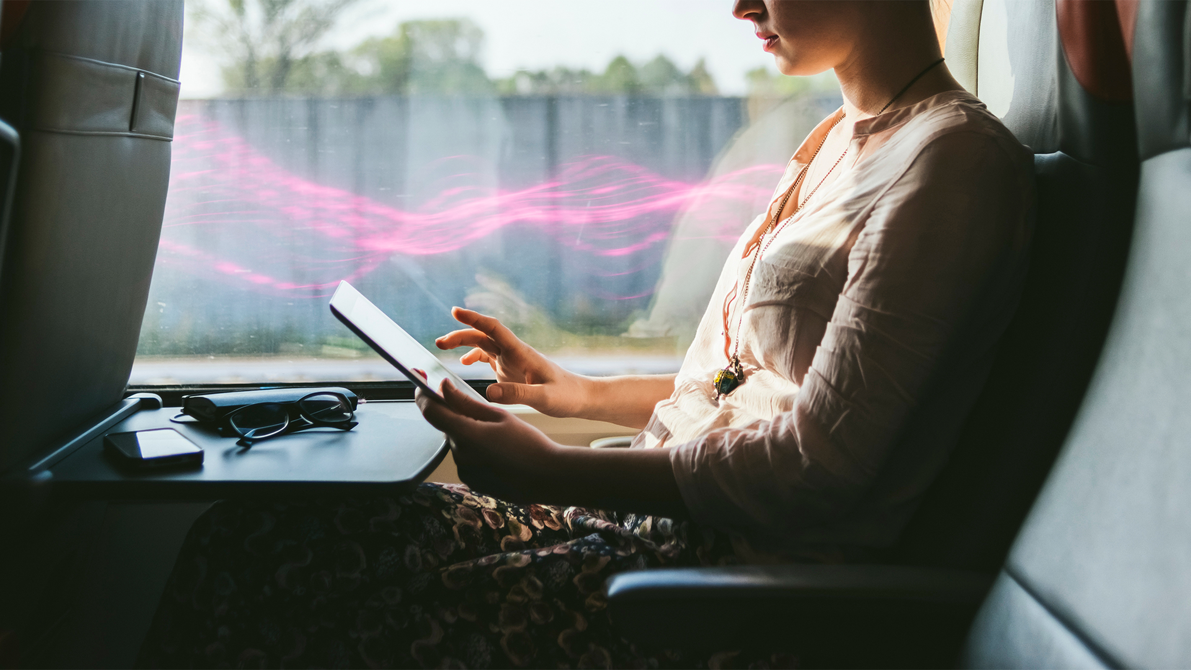 Žena v autobuse so svetelnými efektmi, držiaca tablet s okuliare a mobilom na stolíku.