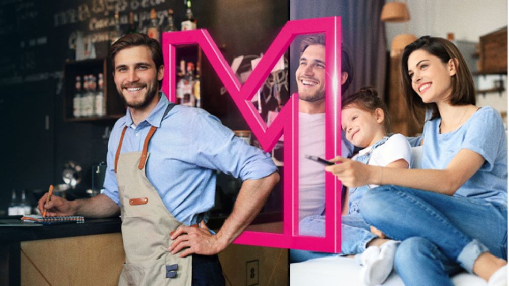 Muž v zástere sa usmieva pri pulte v kaviarni; usmievavá žena a dieťa sedia na gauči s diaľkovým ovládačom, oddelené ružovým rámikom v tvare „M“.