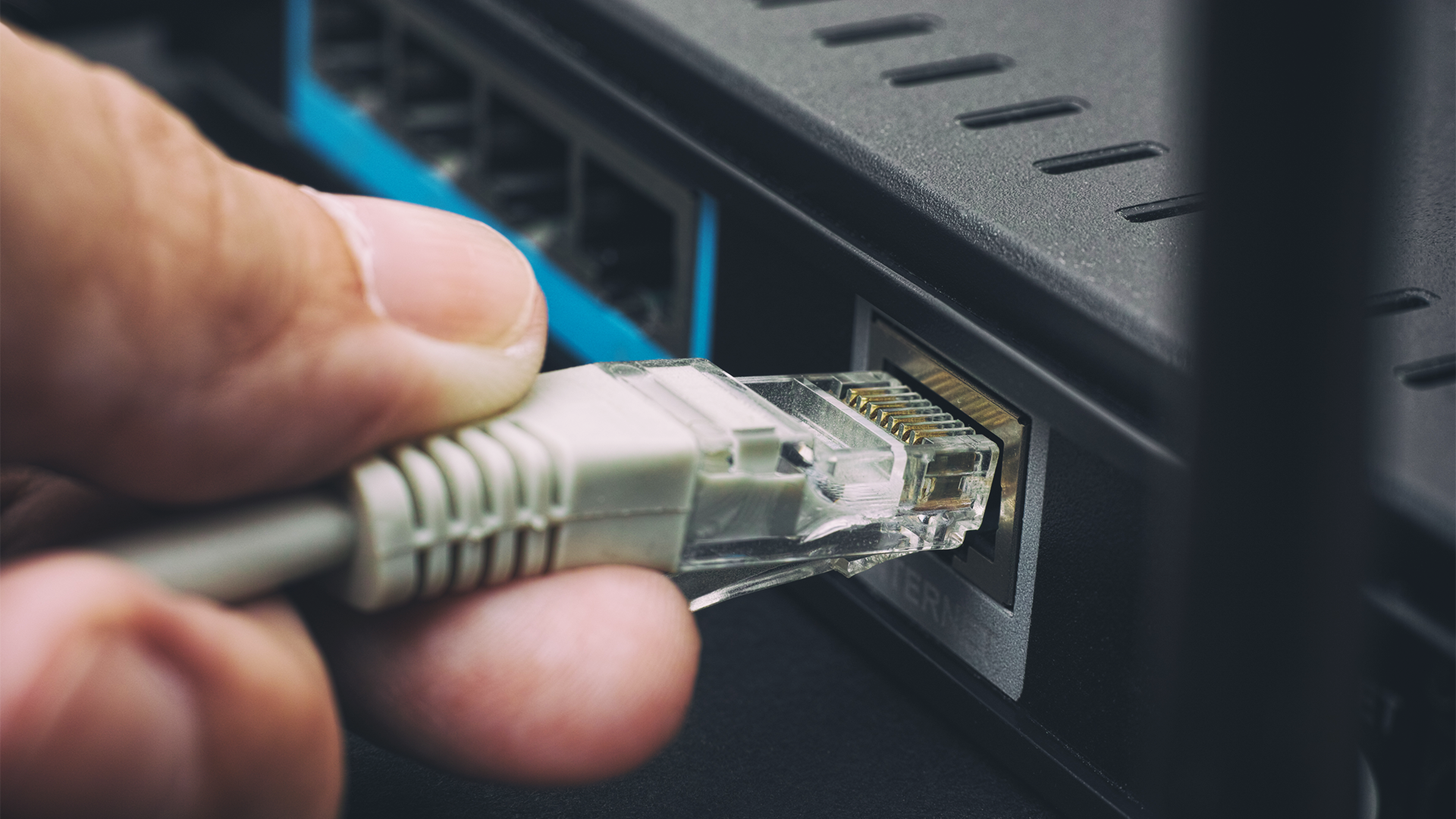 Ruka pripája ethernetový kábel do portu na routeri.