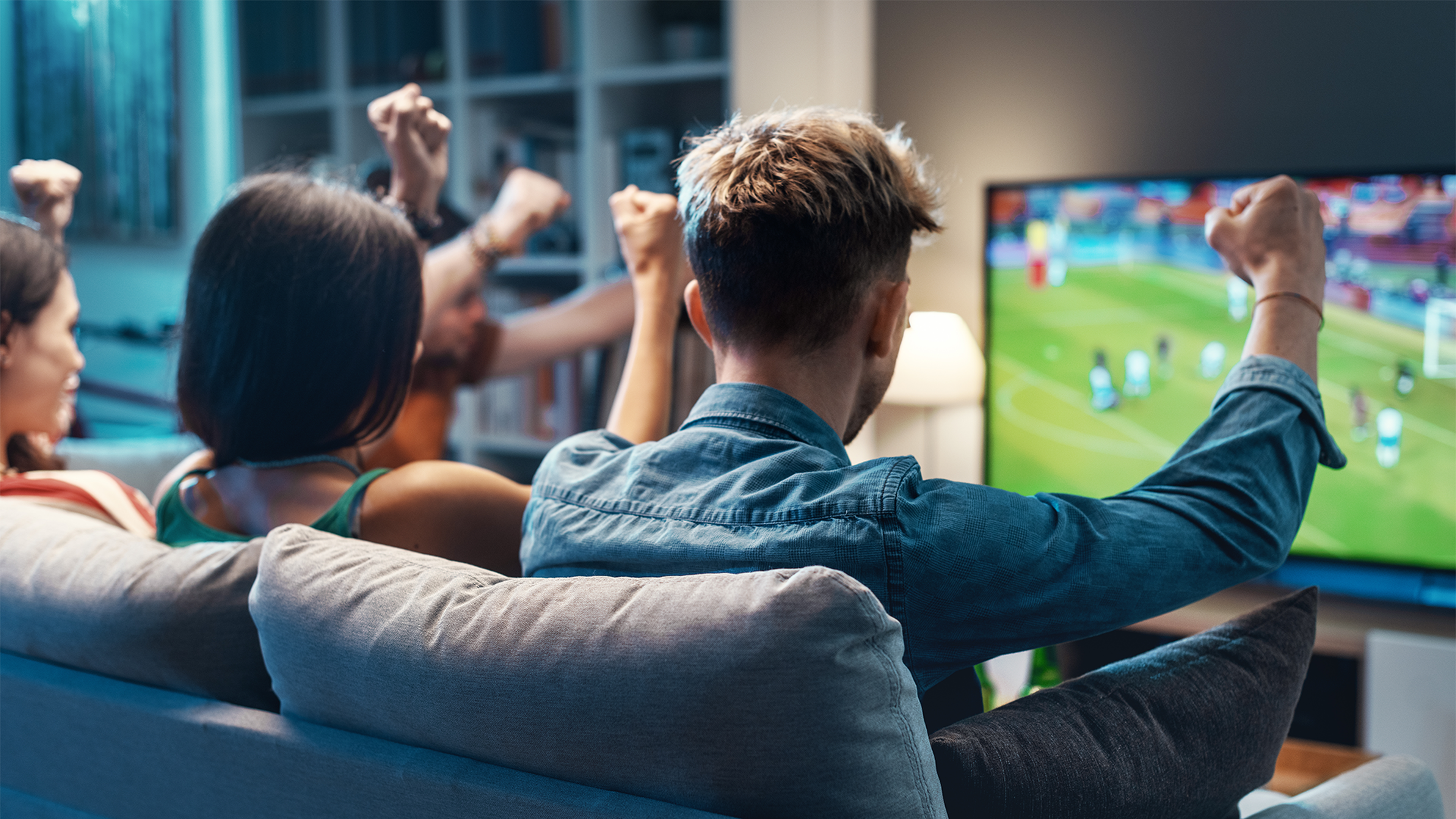 Skupina ľudí sediaca na gauči, nadšene sledujúca futbalový zápas v televízii.