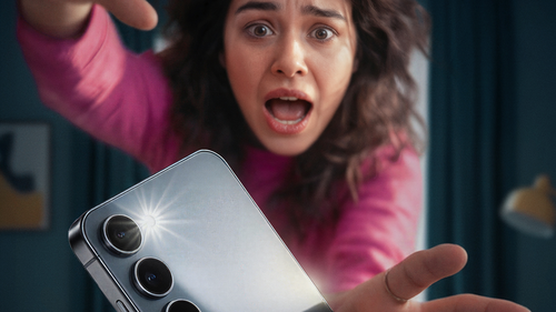 Žena v ružovom svetri sa snaží chytiť padajúci mobilný telefón.