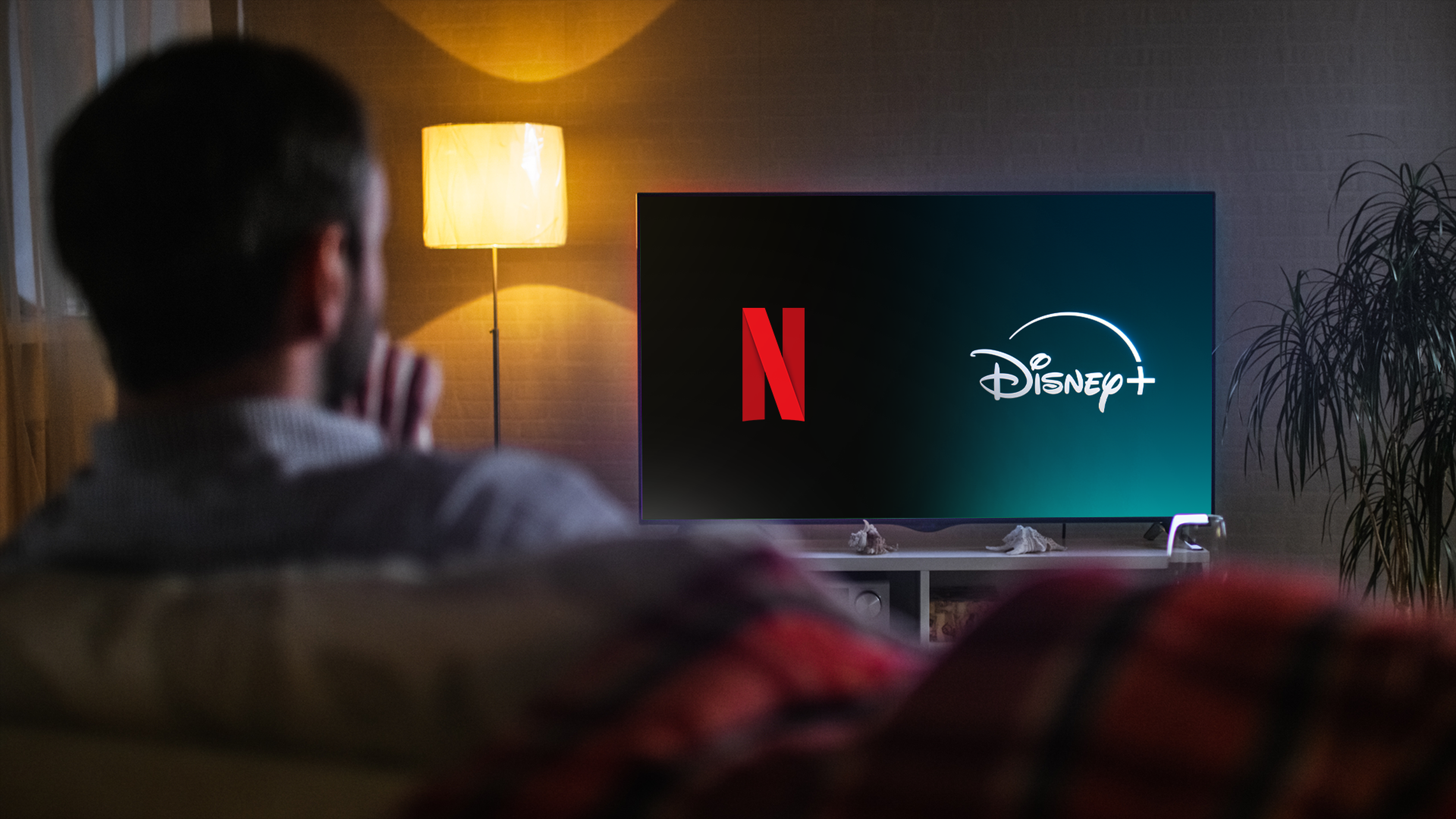 Muž sediaci na gauči sleduje televízor s logami Netflix a Disney+.