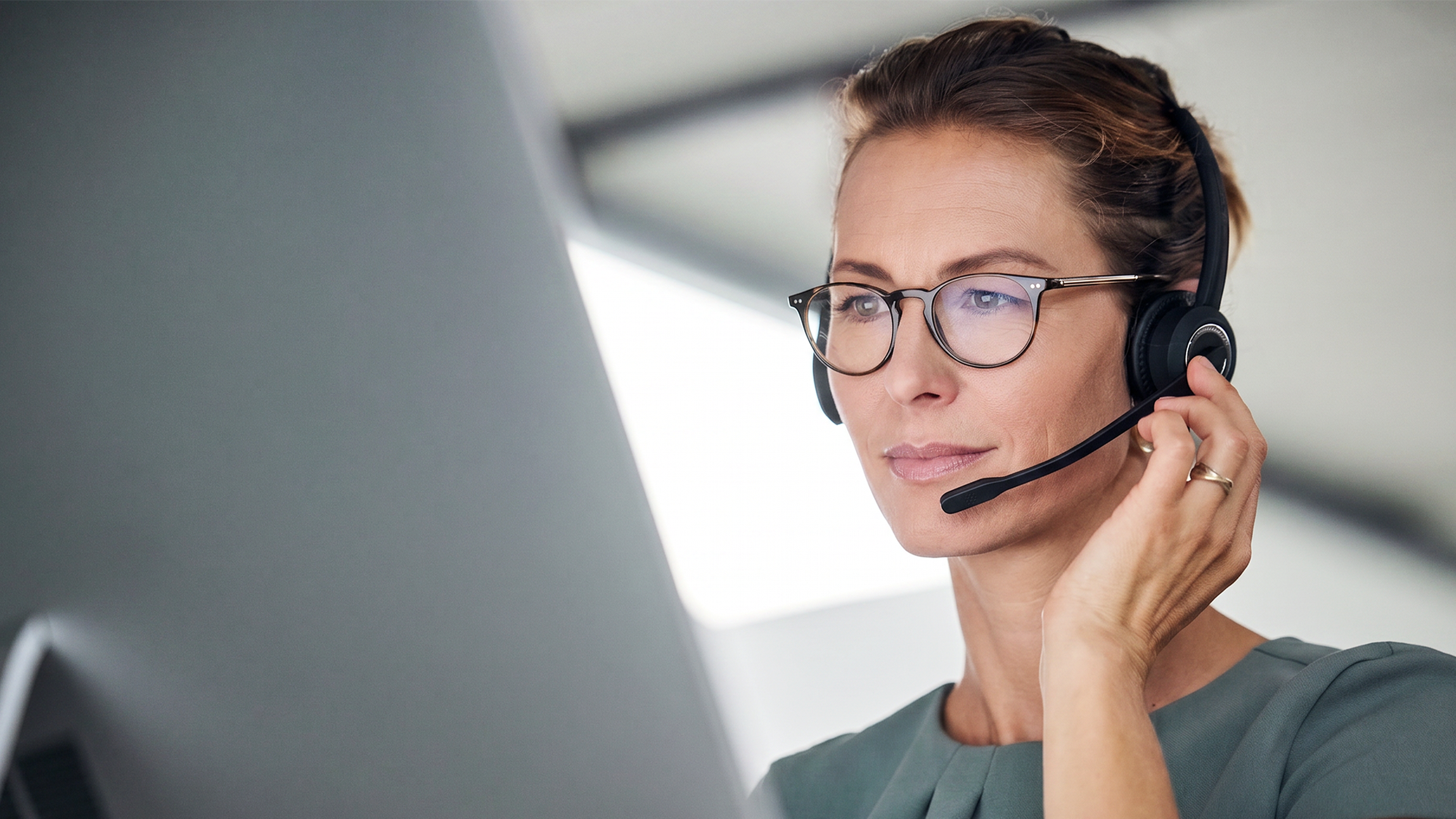 Pracovníčka call centra so slúchadlami, pozerá do obrazovky počítača