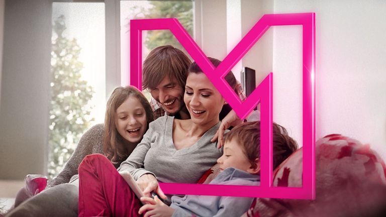 Štvorčlenná rodina sa usmieva a sedí spolu na gauči, obklopená ružovým geometrickým rámom, s jasným oknom v pozadí.