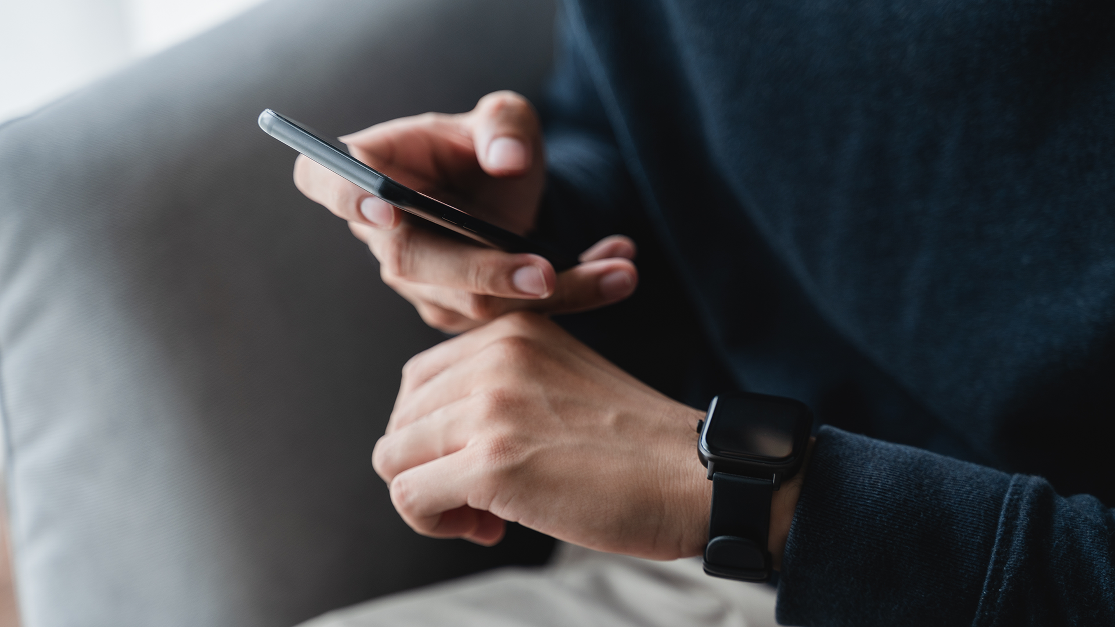 Osoba držiaca mobilný telefón s inteligentnými hodinkami na zápästí.