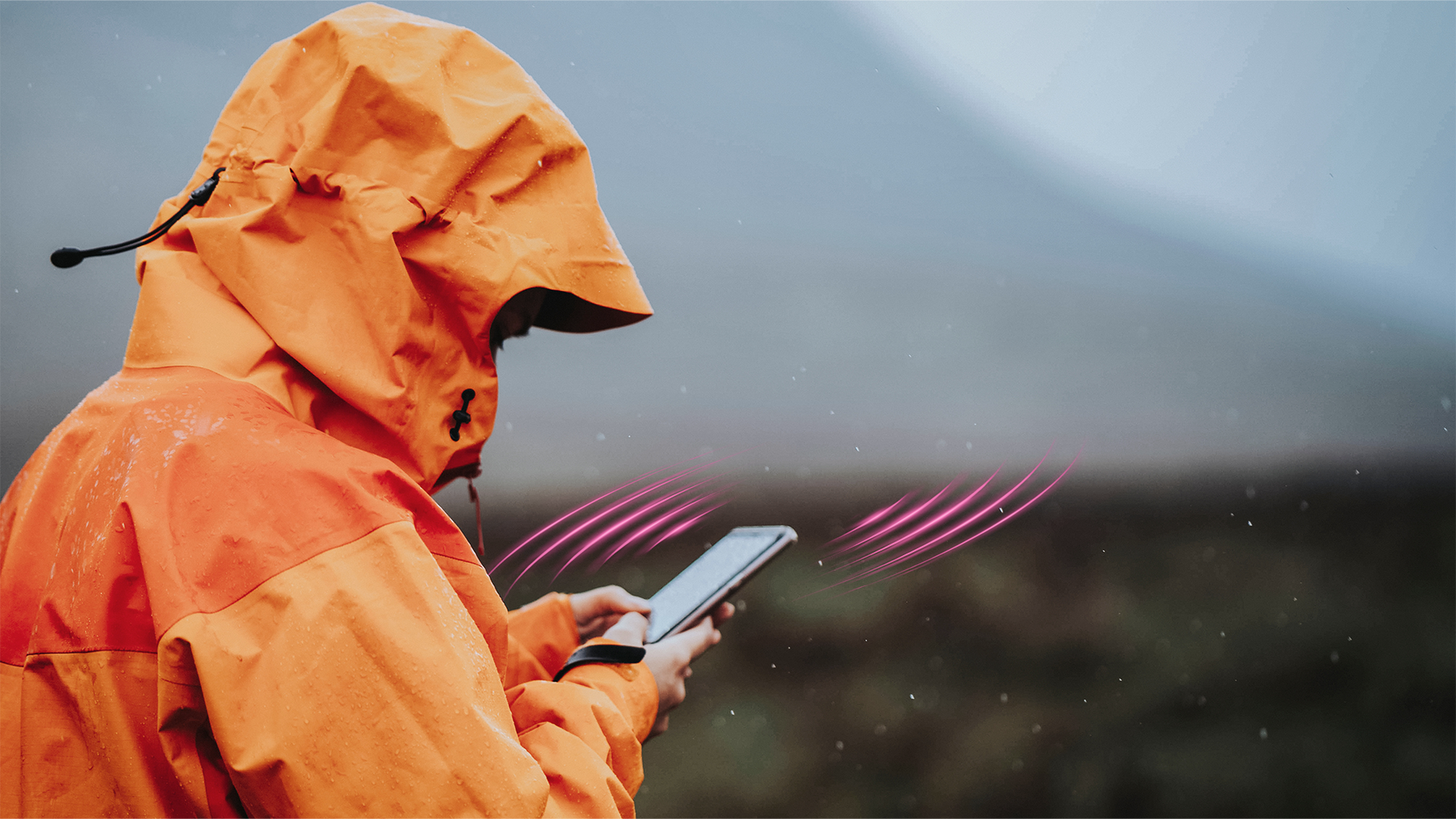 Osoba v oranžovej bunde používa tablet vonku v daždi, so symbolom signálu.