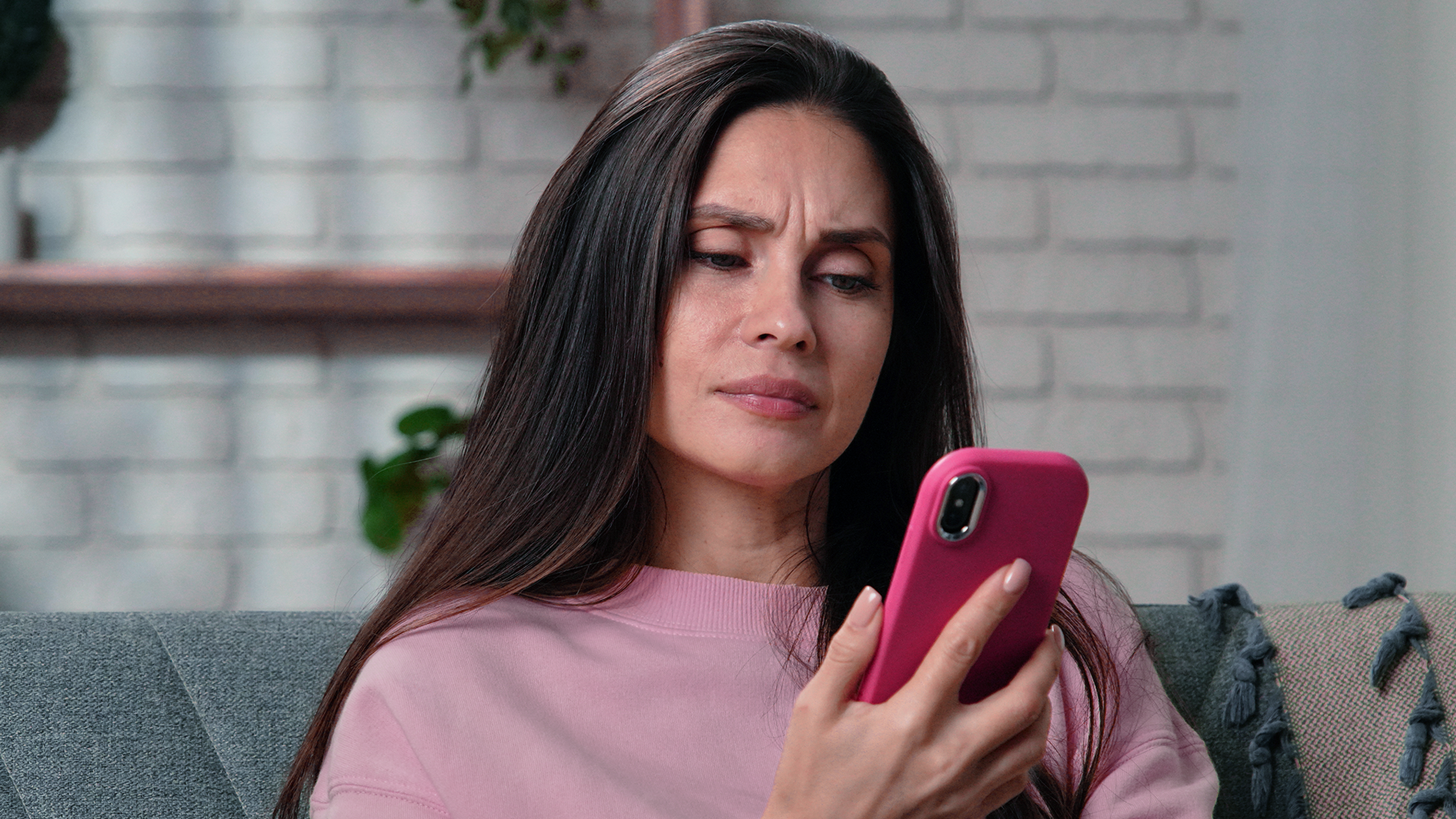 Žena sedí na gauči a sústredene sa pozerá do telefónu