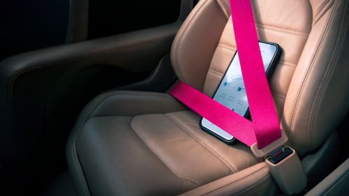 Telefón pripútaný ružovým bezpečnostným pásom na autosedačke a zobrazujúci grafy na obrazovke.