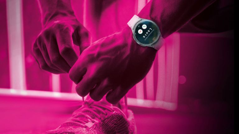 Osoba zaväzujúca si šnúrky na topánke s inteligentnými hodinkami zobrazujúcimi čas pod ružovým osvetlením.