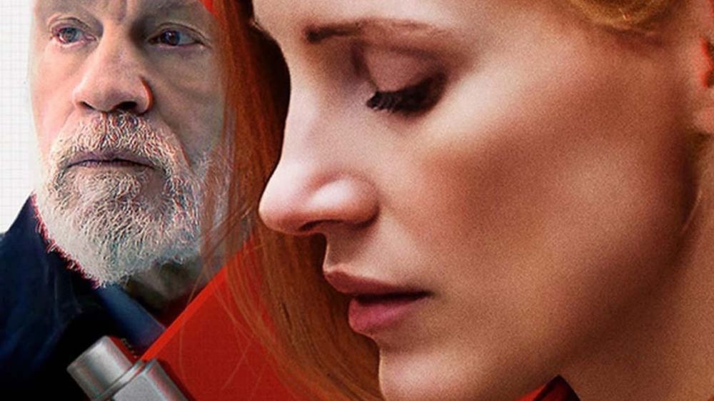 Detailný záber na ženu s ryšavými vlasmi držiacu zbraň, v pozadí bradatý muž. Scéna má dramatickú a intenzívnu atmosféru.