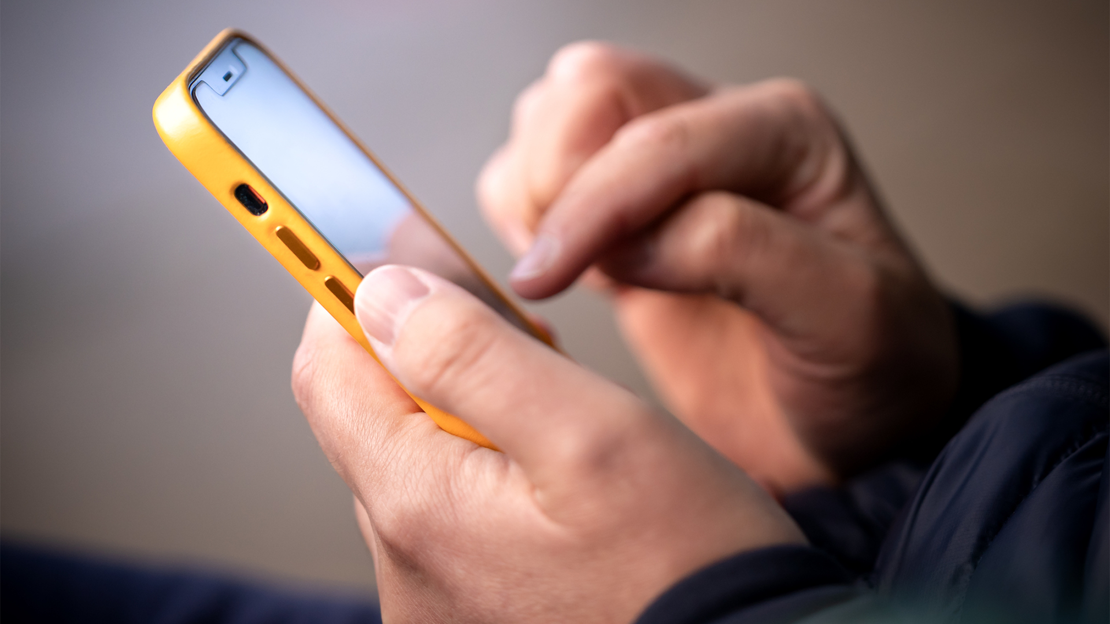 Osoba píše na mobilnom telefóne so žltým obalom.