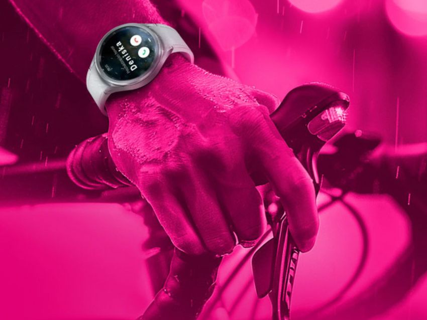 Detailný záber ruky zvierajúcej riadidlá bicykla s inteligentnými hodinkami zobrazujúcimi fitness aplikáciu. Obrázok má ružový odtieň s kvapkami vody.