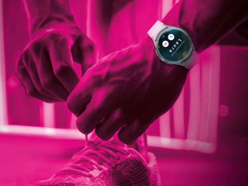 Osoba zaväzujúca si šnúrky na topánke s inteligentnými hodinkami zobrazujúcimi čas pod ružovým osvetlením.