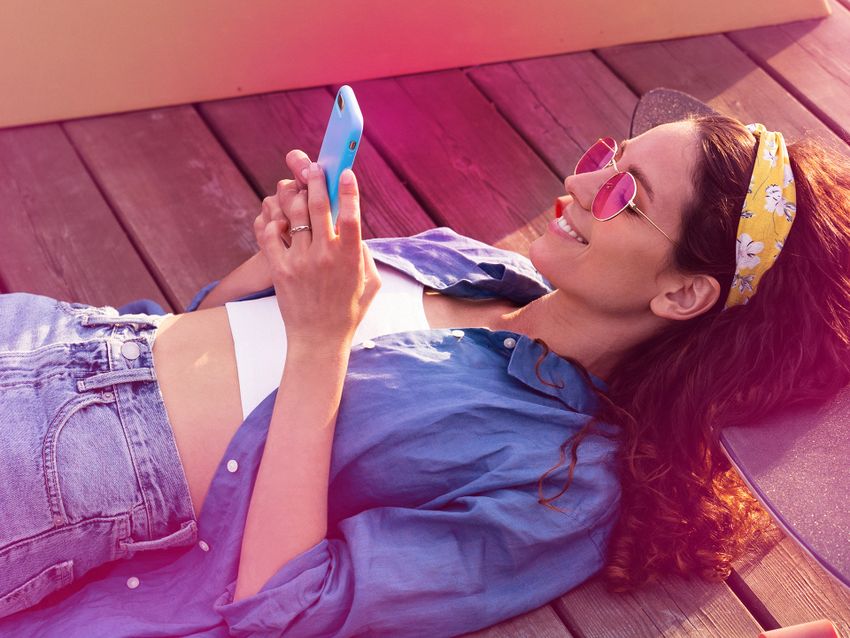 mladá usmiata brunetka ležiaca v lete vonku na slnku pozerá do mobilu