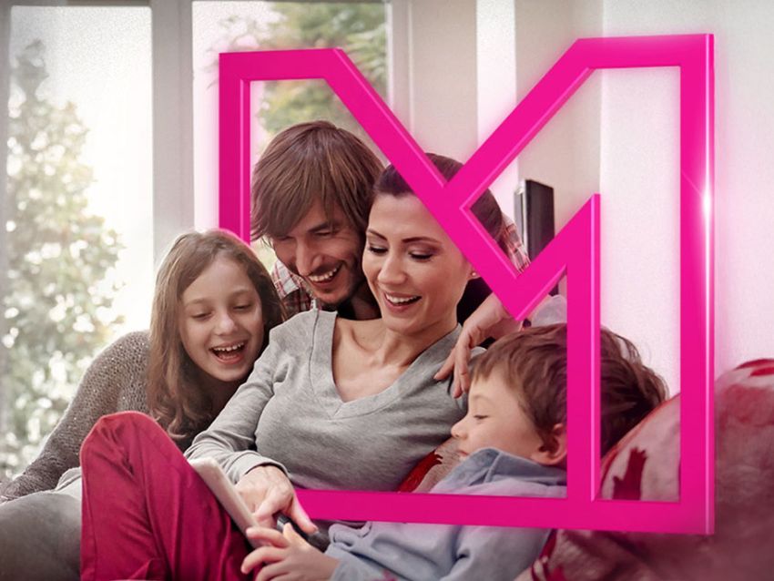 Štvorčlenná rodina sa usmieva a sedí spolu na gauči, obklopená ružovým geometrickým rámom, s jasným oknom v pozadí.