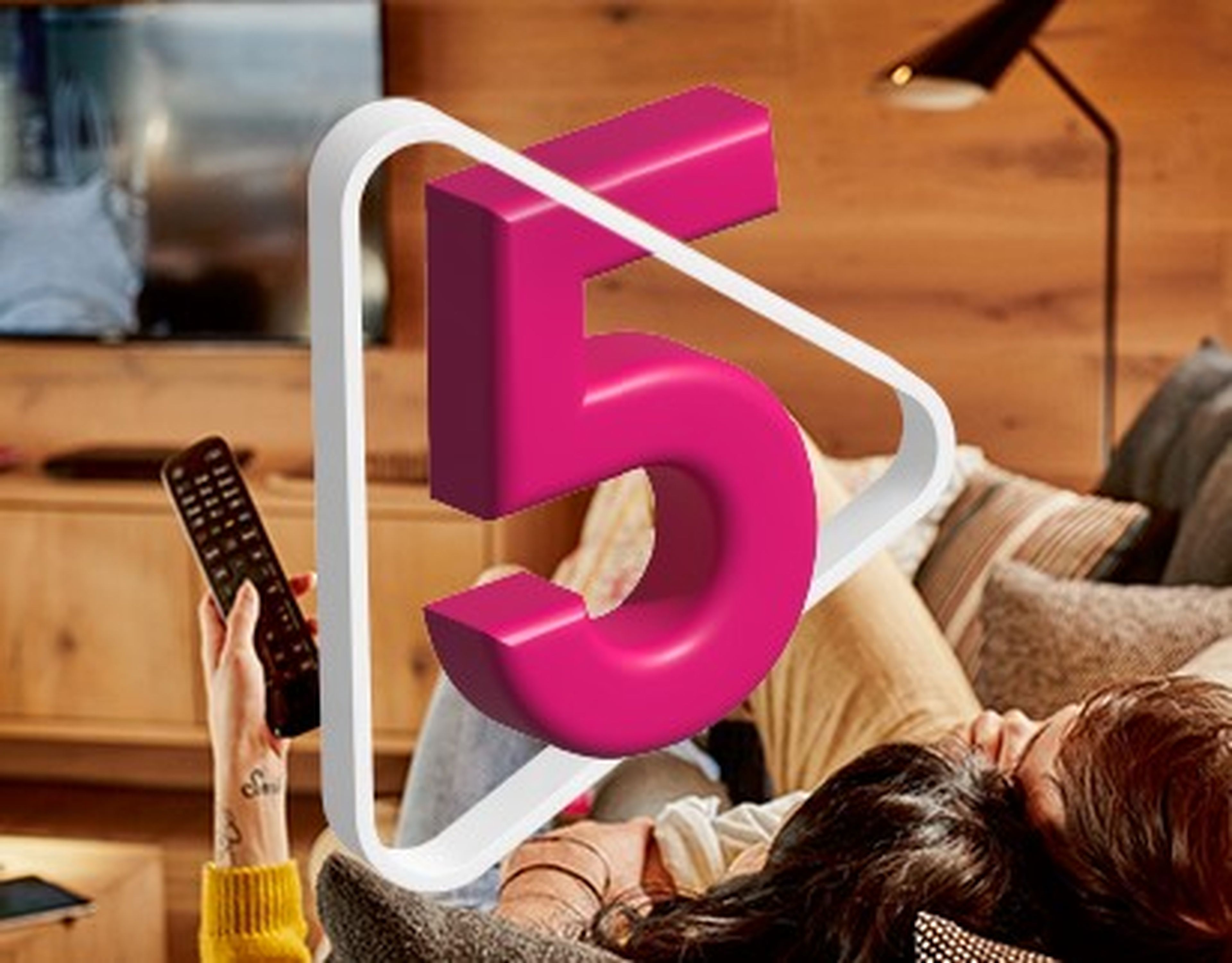 Osoba držiaca diaľkové ovládanie televízora relaxuje na gauči. Na obrázku je zobrazené veľké ružové 3D číslo 5.