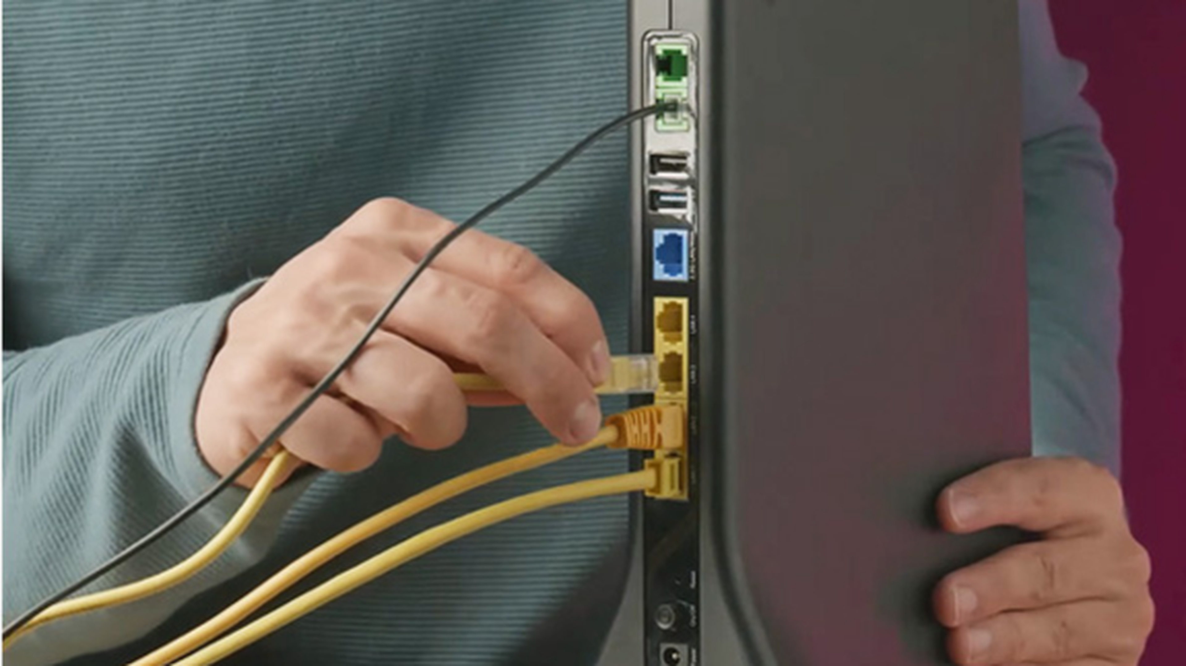 Osoba pripája žlté ethernetové káble k zadnej strane čierneho routera s viditeľnými rôznymi portami.