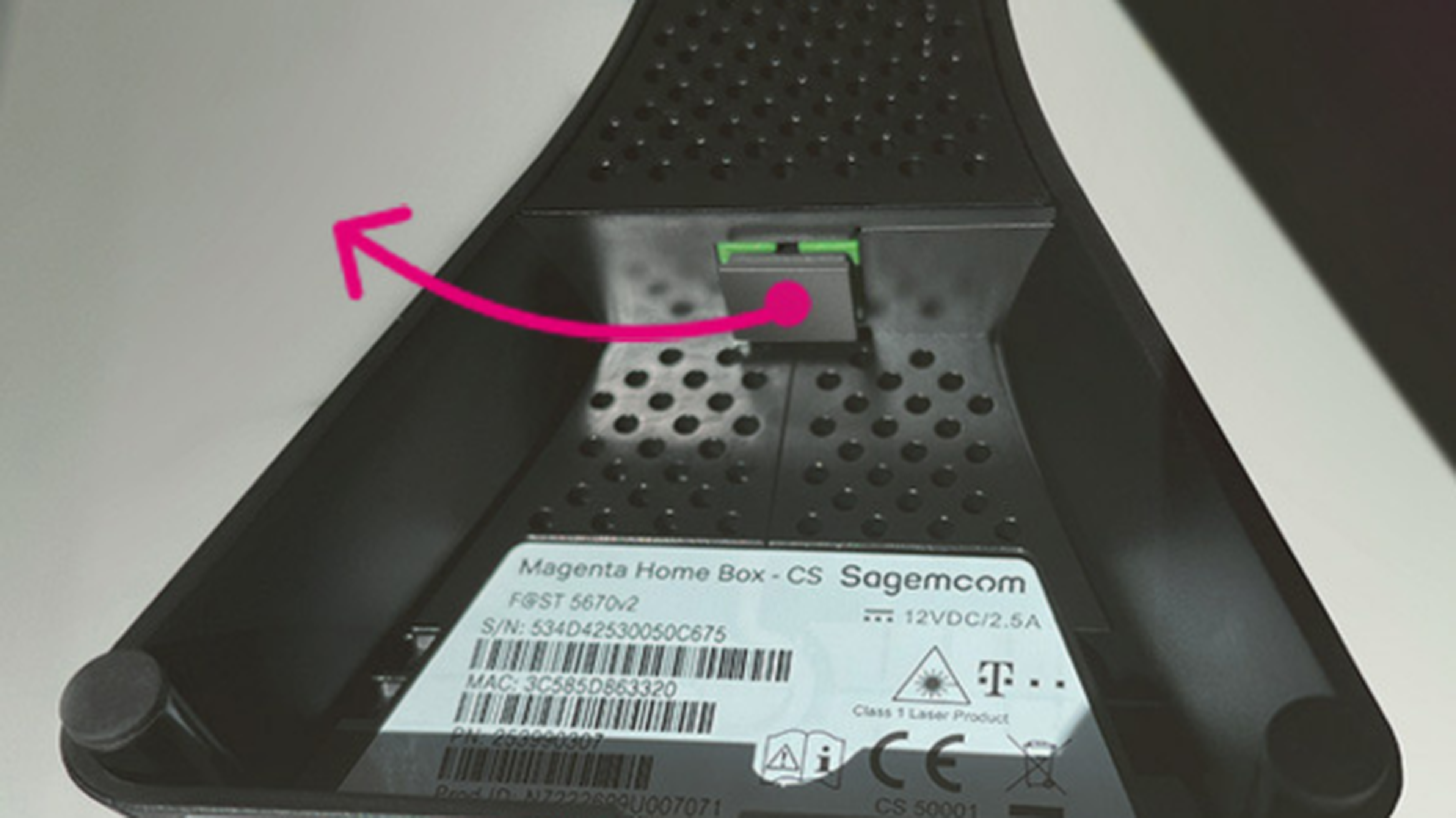 Detail spodnej strany Sagemcom Magenta Home Box, s ružovou šípkou zvýrazneným tlačidlom reset. Viditeľné sú štítky a sériové číslo.