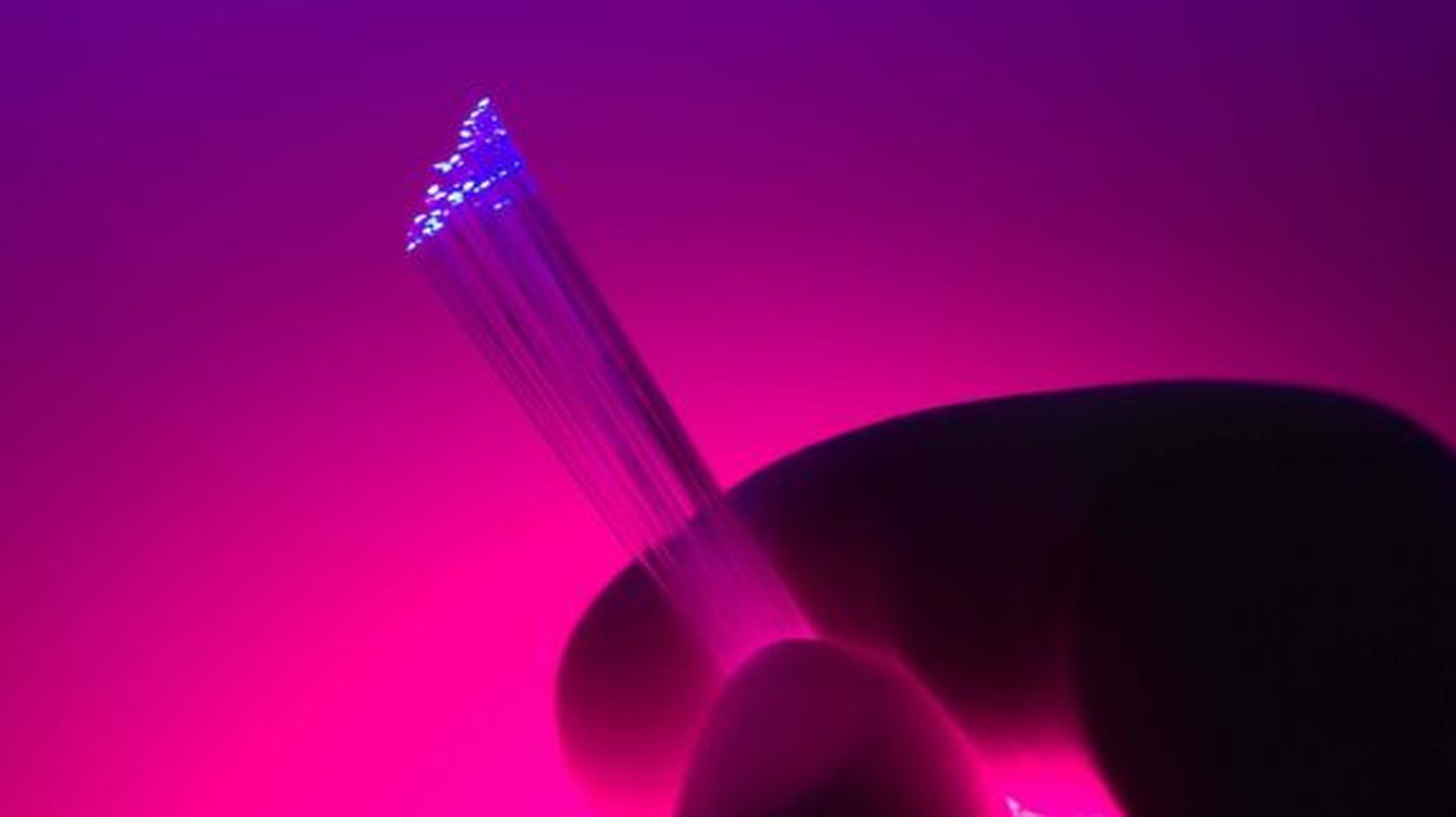 Naše technológie pomáhajú Detailný záber ruky držiacej žiariace optické vlákna na žiarivo ružovom a fialovom pozadí.