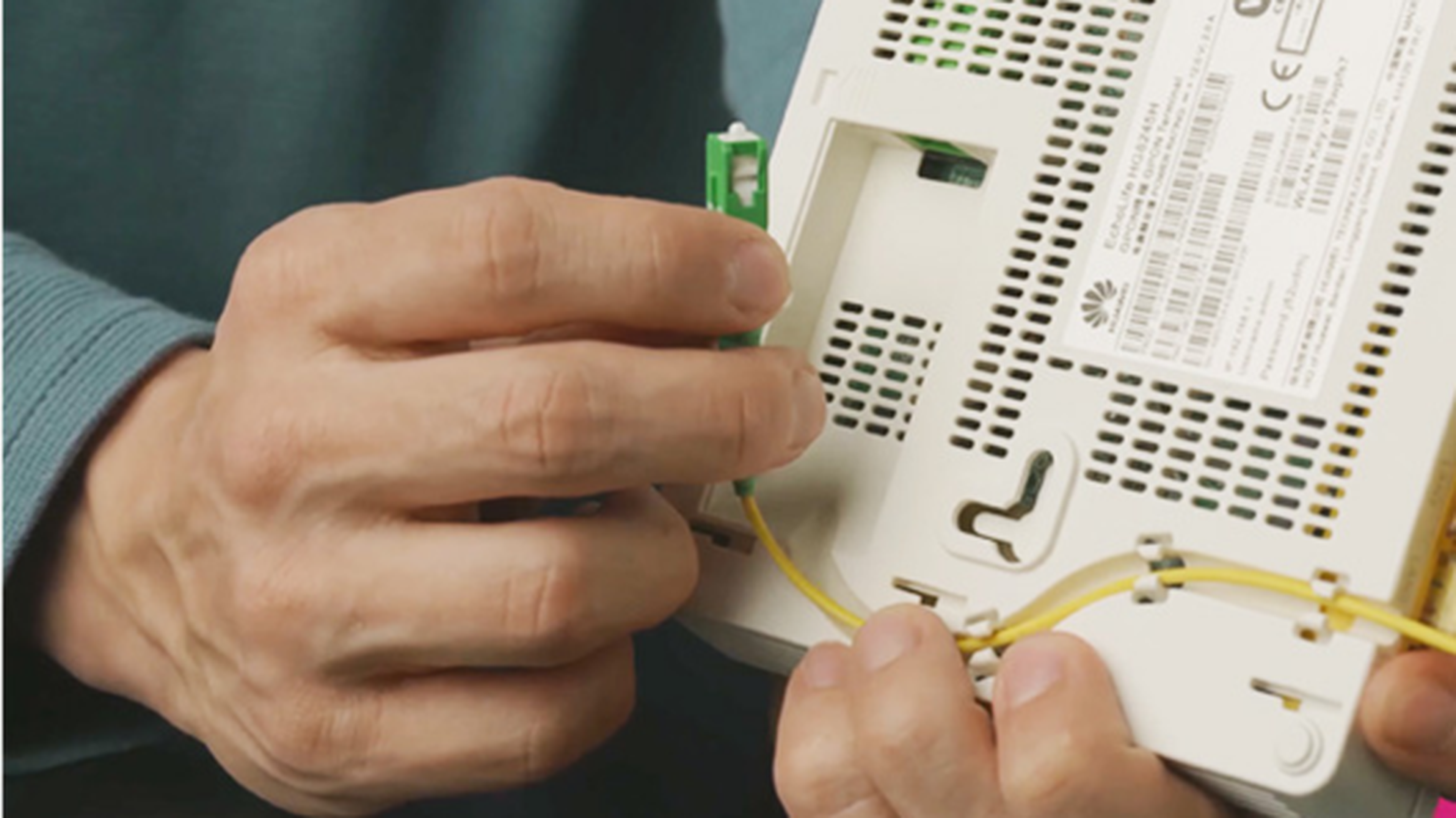 Ruky pripájajúce žltý optický kábel k bielemu sieťovému zariadeniu, demonštrujúce technické nastavenie a konektivitu.