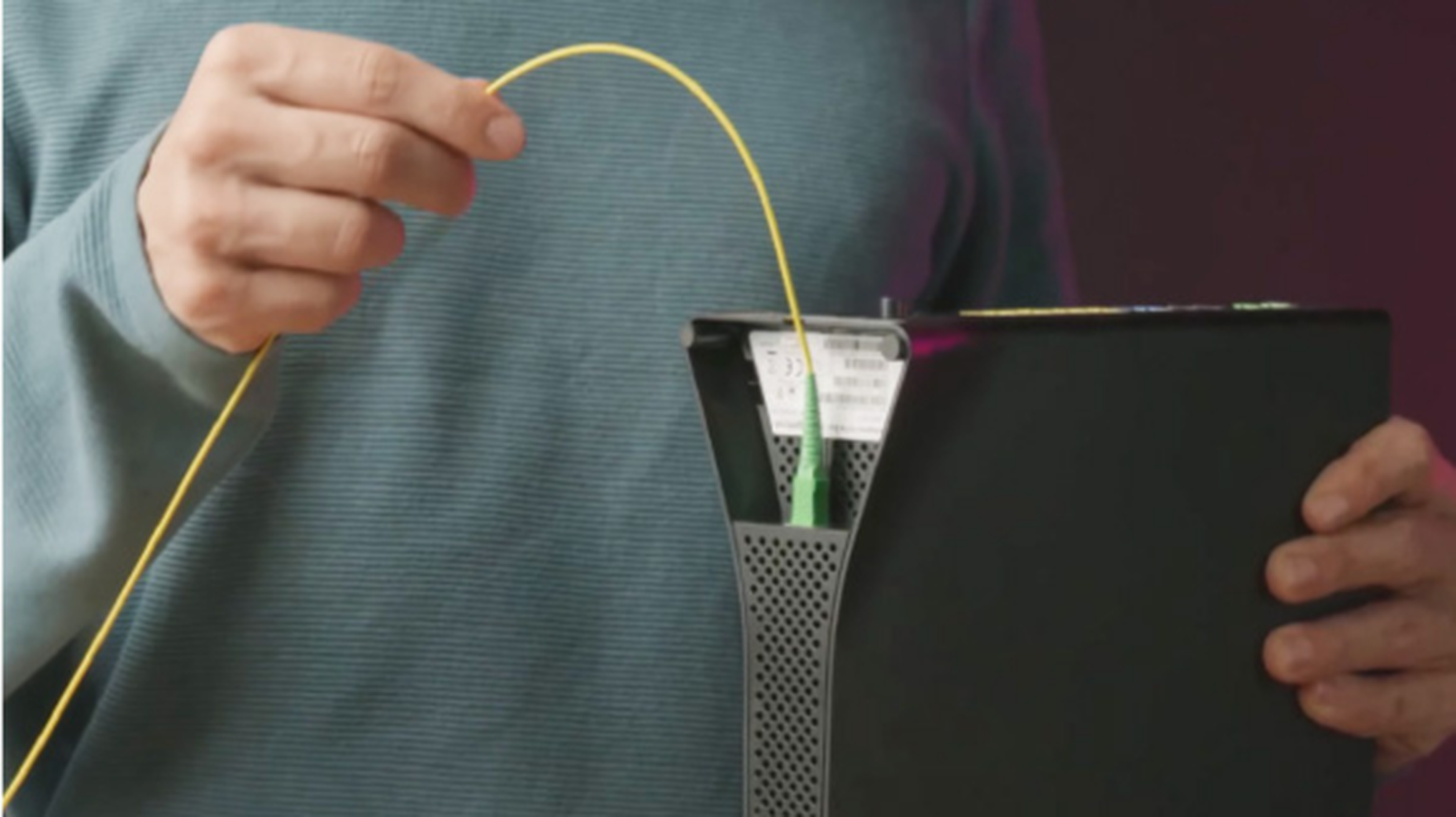 Osoba, ktorá má na sebe modré tričko s dlhým rukávom a pripája žltý optický kábel k čiernemu modemu.