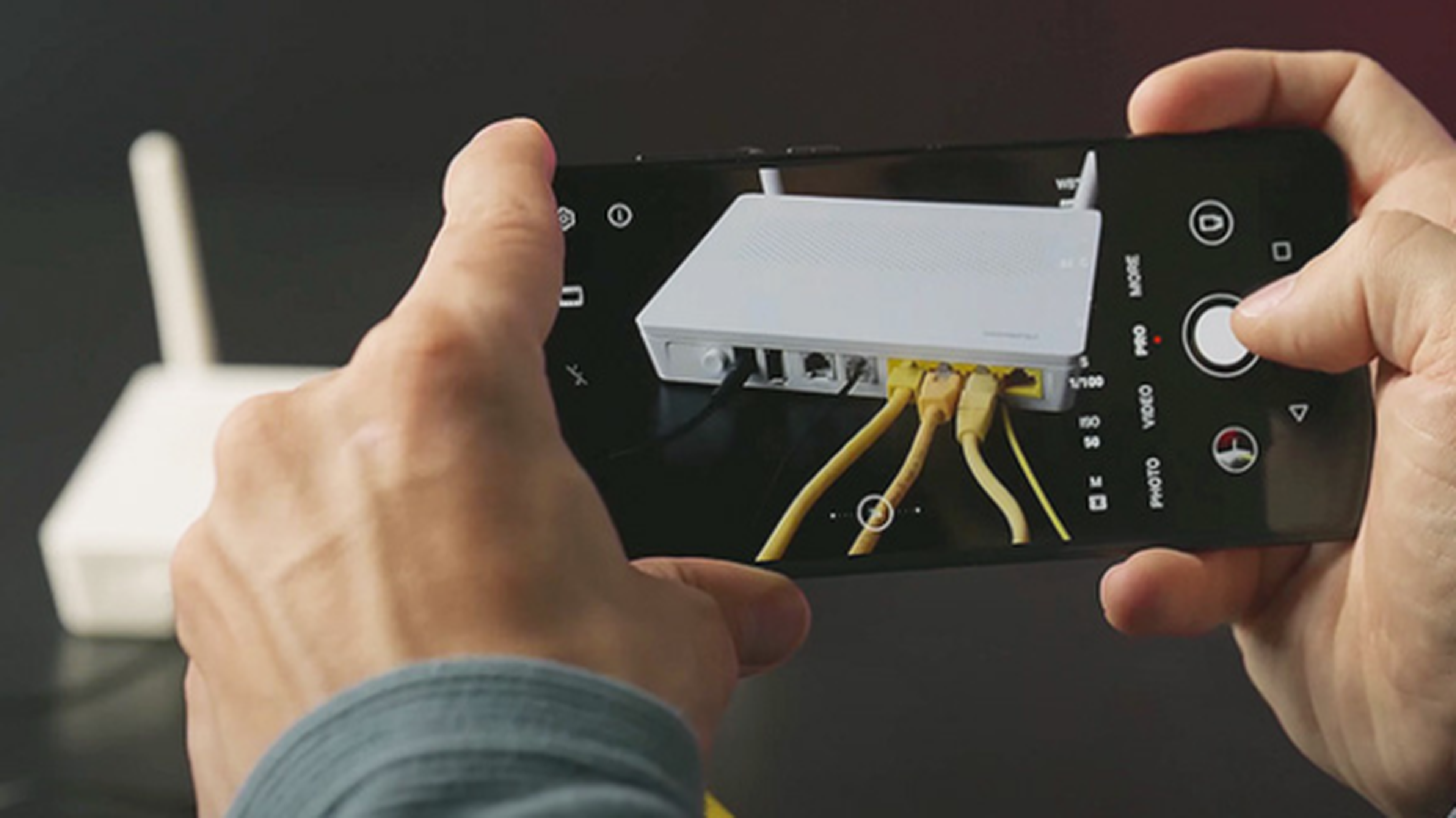 Osoba fotografujúca biely router so žltými káblami pomocou smartfónu.