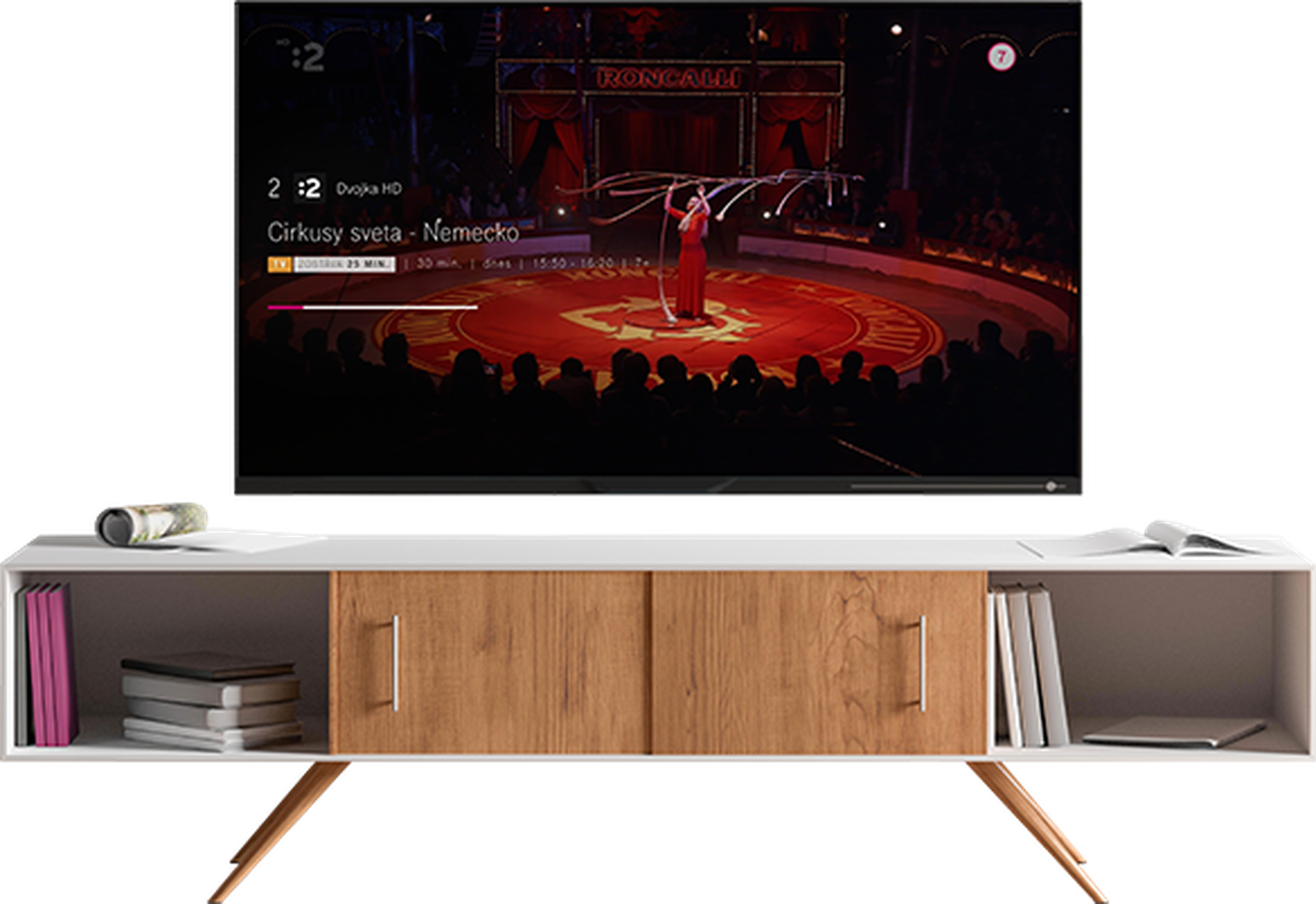Televízor na modernom stojane premietajúci cirkusové predstavenie s umelcom v červenom na pódiu, obklopeným publikom.