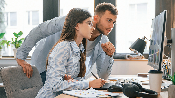 Dvaja kolegovia v marketingu intenzívne spolupracujú nad návrhom na veľkom monitore - reprezentuje prácu v reálnom čase cez cloudové služby.