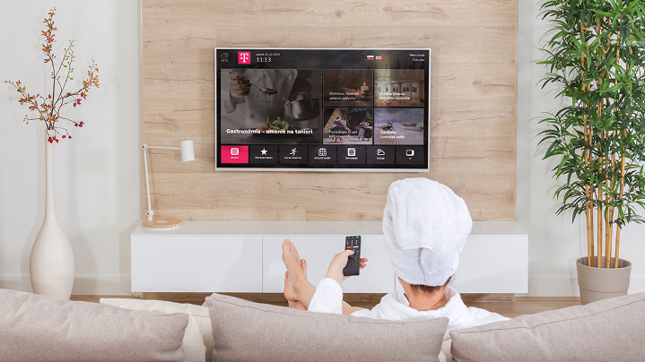 Hotelový hosť sleduje televíziu z postele - demonštruje využitie TV ako súčasť zákazníckej skúsenosti v hoteli.