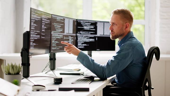 IT špecialista pracuje na viacerých monitoroch v technologickom prostredí - zdôrazňuje spoľahlivú konektivitu a zabezpečenie siete.