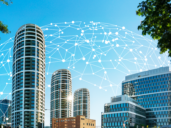 Moderné kancelárske budovy s digitálnou vizualizáciou siete nad nimi. Symbolizujú prepojenie IoT zariadení a zber dát v reálnom čase pre efektívnejšie podnikanie.