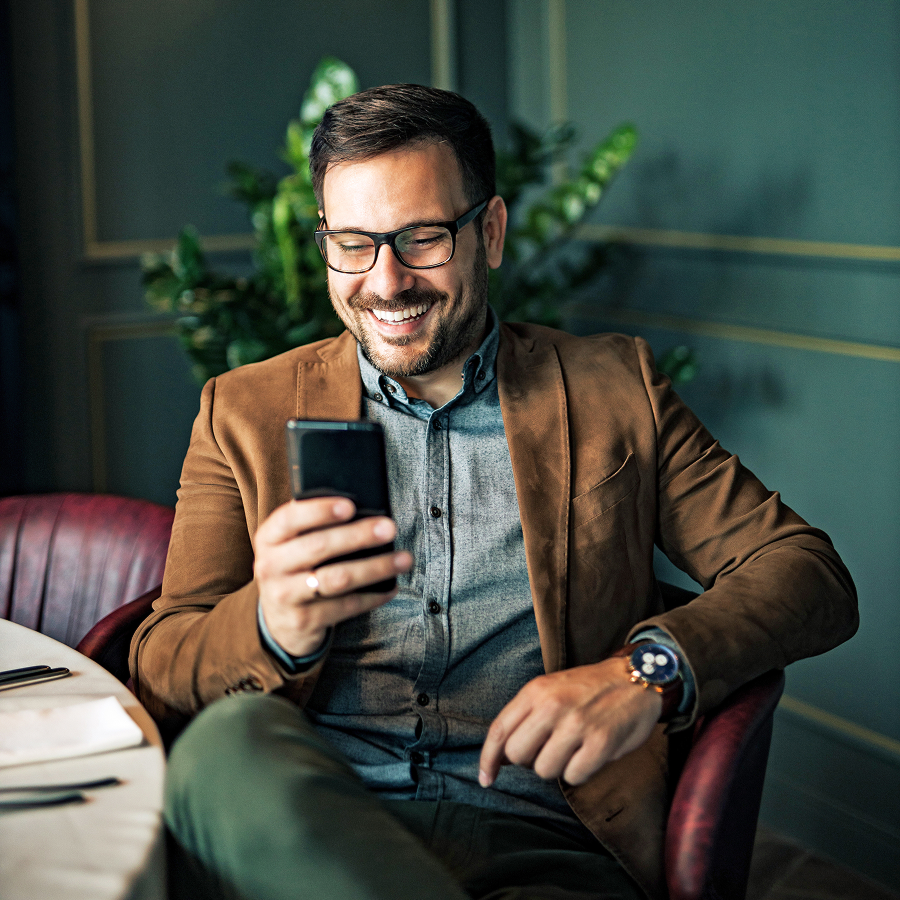 Sediaci muž číta SMS správu na mobilnom telefóne – vizuál služby Telekom SMS & RCS Messaging.